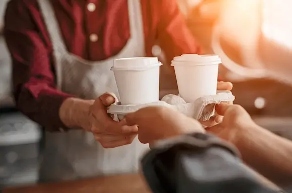 Barista handing over two takeaway coffees in a cardboard holder.