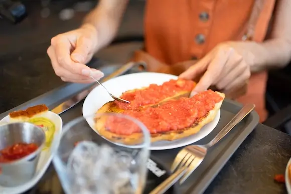Person preparing tostada with fresh tomato, a classic Spanish breakfast dish.