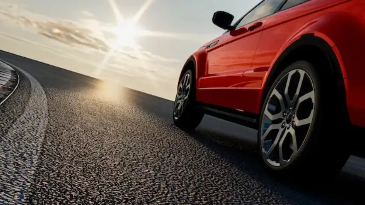 Red car driving along a curved road at sunset, close-up of wheel and body.