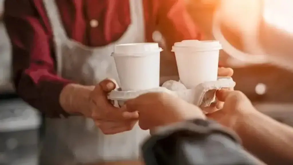 Barista handing over two takeaway coffees in a cardboard holder.