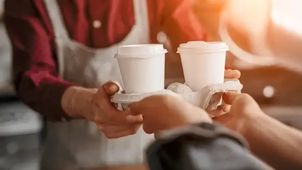 Barista handing over two takeaway coffees in a cardboard holder.