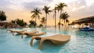 Luxury hotel infinity pool with sun loungers, palm trees and a sunset view over the Mediterranean.