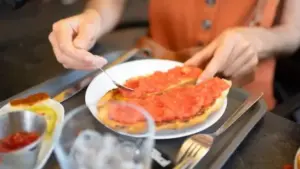 Person preparing tostada with fresh tomato, a classic Spanish breakfast dish.