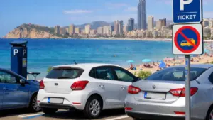 Am Strand von Benidorm geparkte Autos, die typische Parkplätze und die Skyline der Küstenstadt zeigen